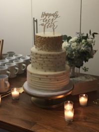 Three-tiered cake with white frosting and gold decorations with Happily Ever After topper